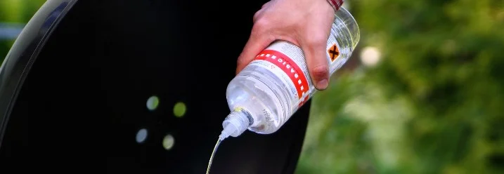 Person gießt Flüssigkeit in Grill